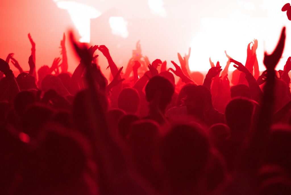 Concert crowd with raised arms applauding and partying at music festival in red stage lights